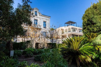 Deux fauteuils en rotin et une table basse avec une tasse, sur une terrasse donnant sur un jardin verdoyant.