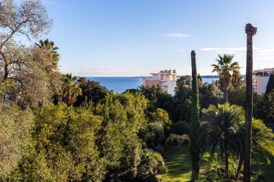 Deux fauteuils en rotin et une table basse avec une tasse, sur une terrasse donnant sur un jardin verdoyant.