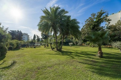 Deux fauteuils en rotin et une table basse avec une tasse, sur une terrasse donnant sur un jardin verdoyant.