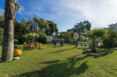 Deux fauteuils en rotin et une table basse avec une tasse, sur une terrasse donnant sur un jardin verdoyant.