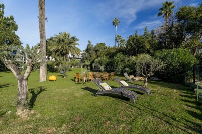 Deux fauteuils en rotin et une table basse avec une tasse, sur une terrasse donnant sur un jardin verdoyant.