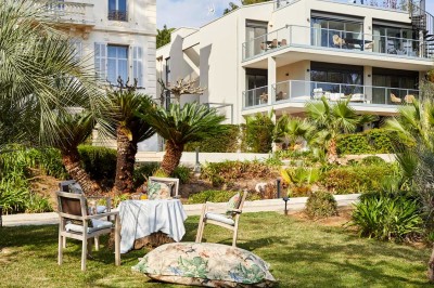 Deux fauteuils en rotin et une table basse avec une tasse, sur une terrasse donnant sur un jardin verdoyant.