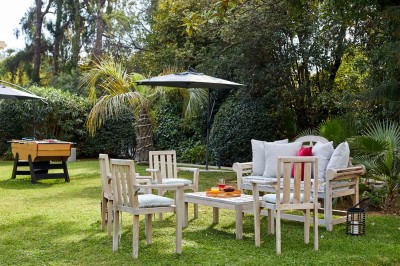Deux fauteuils en rotin et une table basse avec une tasse, sur une terrasse donnant sur un jardin verdoyant.