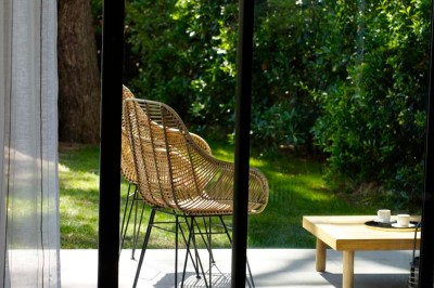 Deux fauteuils en rotin et une table basse avec une tasse, sur une terrasse donnant sur un jardin verdoyant.