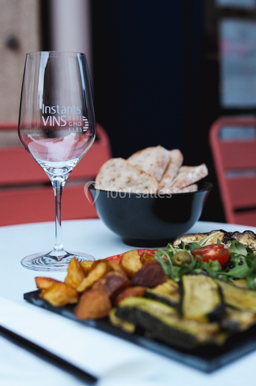 Verre de vin vide, assiette de légumes grillés et pommes de terre, avec un bol de pain sur une table en extérieur.