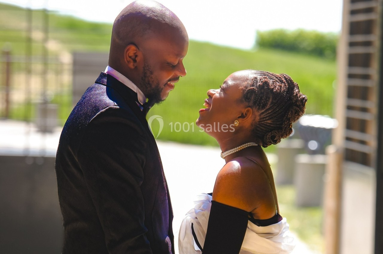 Un couple élégant échange un moment complice en extérieur, sous une lumière naturelle et un décor verdoyant.