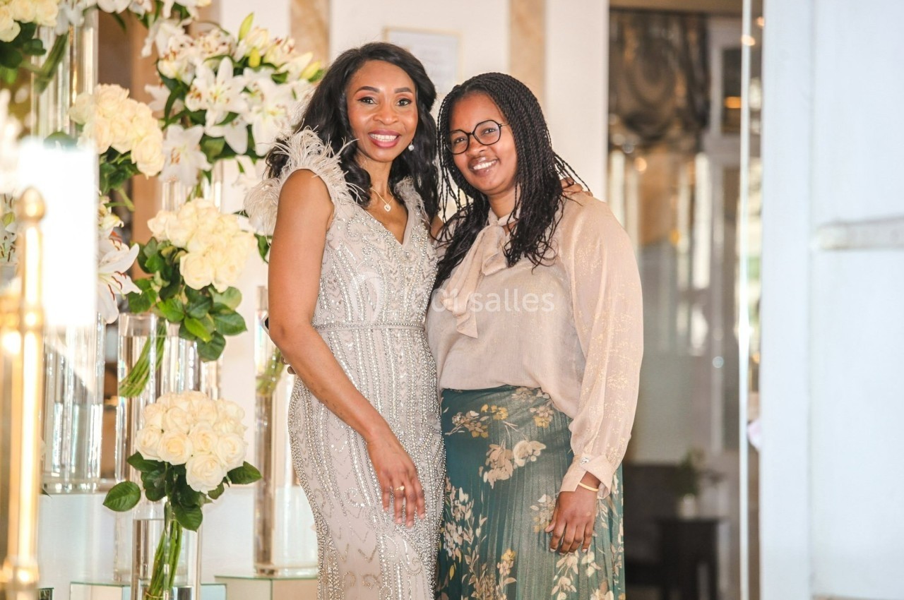 Deux femmes souriantes posent devant une décoration florale composée principalement de roses blanches.