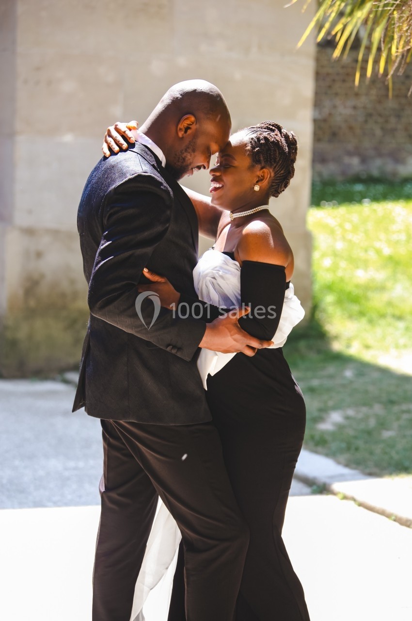 Un couple élégant s'enlace tendrement en extérieur, sous une lumière naturelle.
