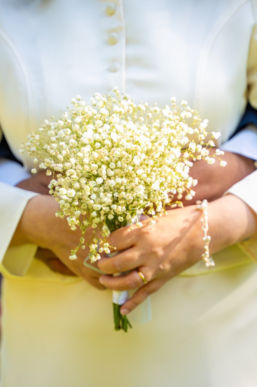 Gros plan sur un bouquet de gypsophile blanc tenu à deux mains, avec une alliance dorée à un doigt, sur une tenue claire.