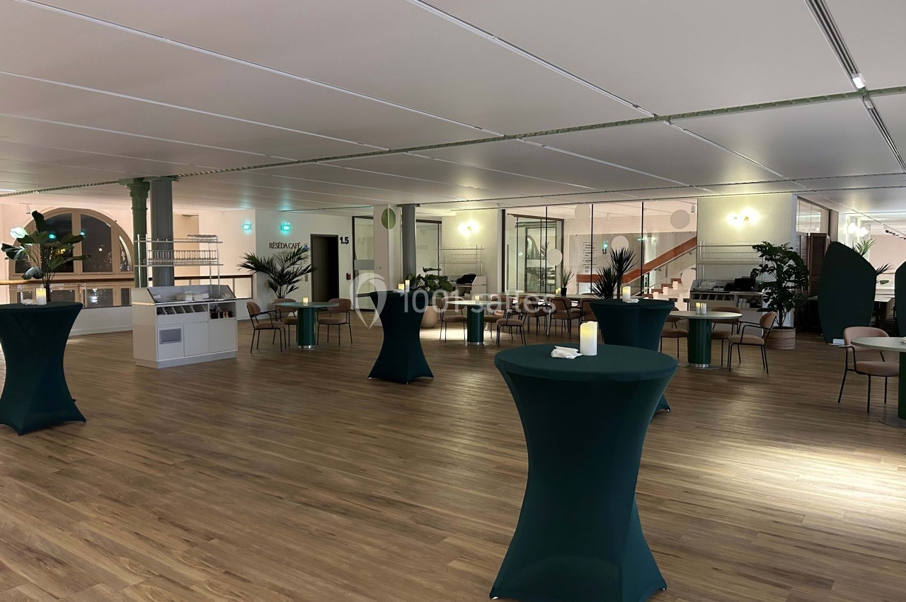 Salle spacieuse avec parquet, tables hautes recouvertes de nappes vertes et décoration végétale moderne.