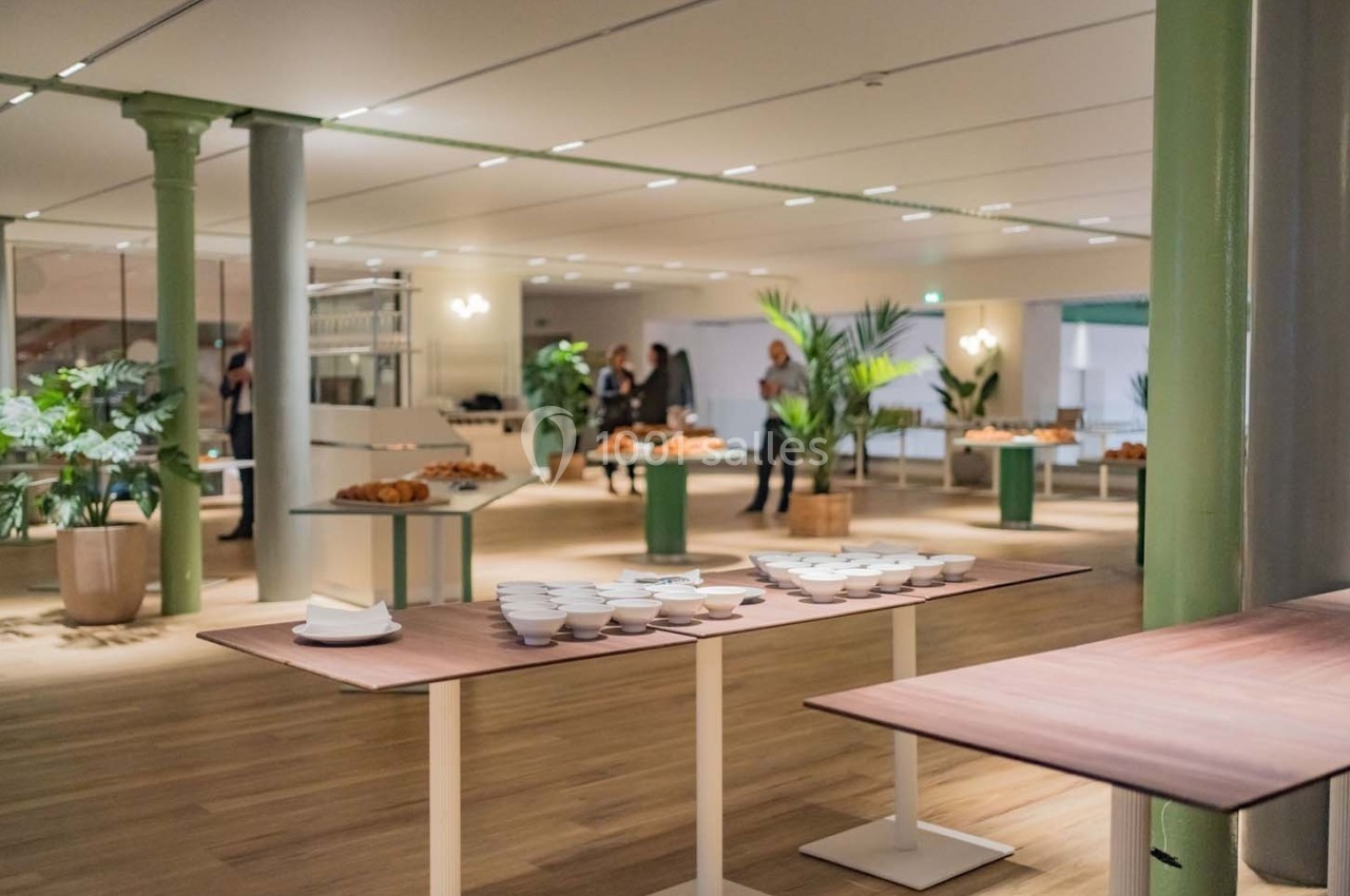 Salle lumineuse avec tables en bois, vaisselle blanche, viennoiseries et plantes décoratives en arrière-plan.