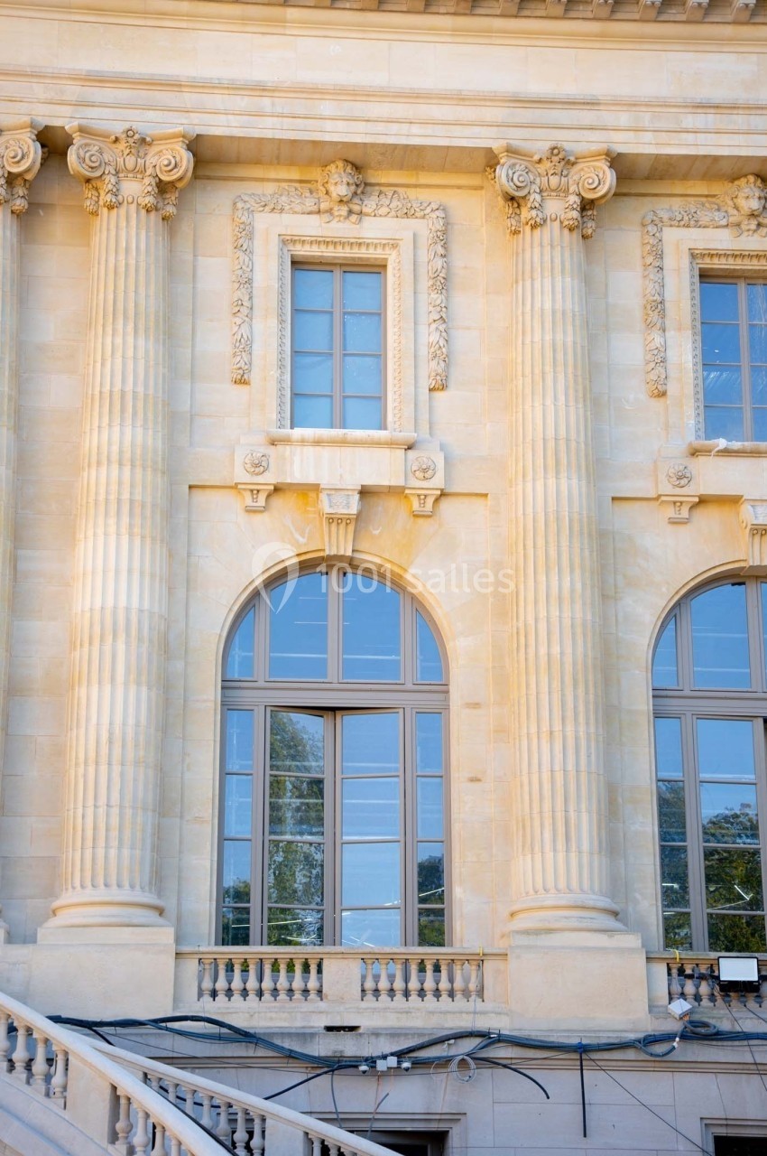 Façade en pierre avec colonnes classiques, fenêtres à arcs cintrés et détails sculptés.