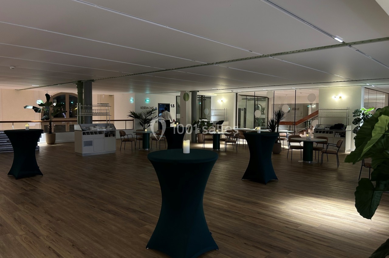 Salle de réception avec tables hautes couvertes de nappes vertes, éclairage tamisé et décorations végétales.