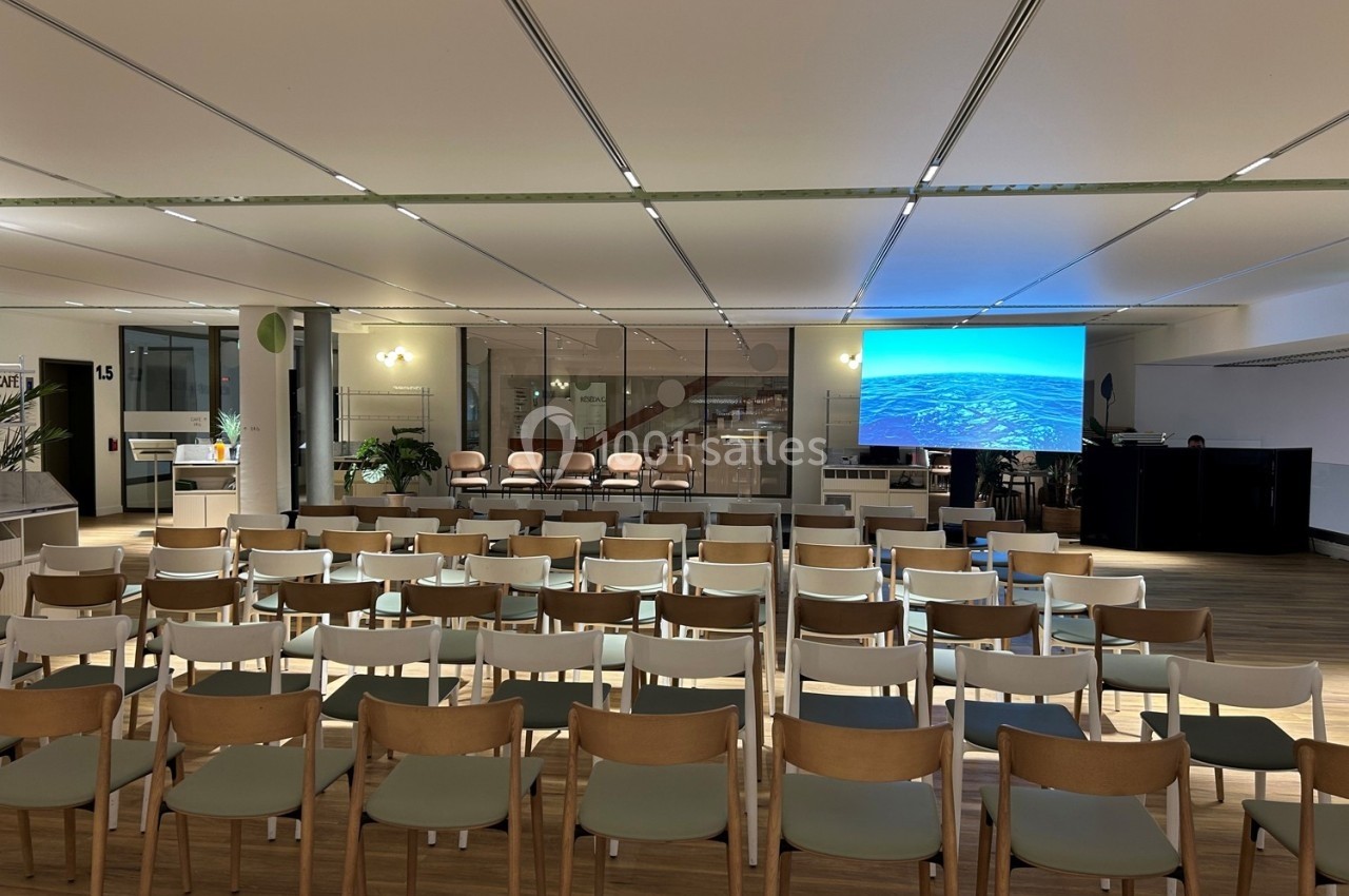 Salle de conférence avec des rangées de chaises vides face à un écran allumé affichant une image aérienne.