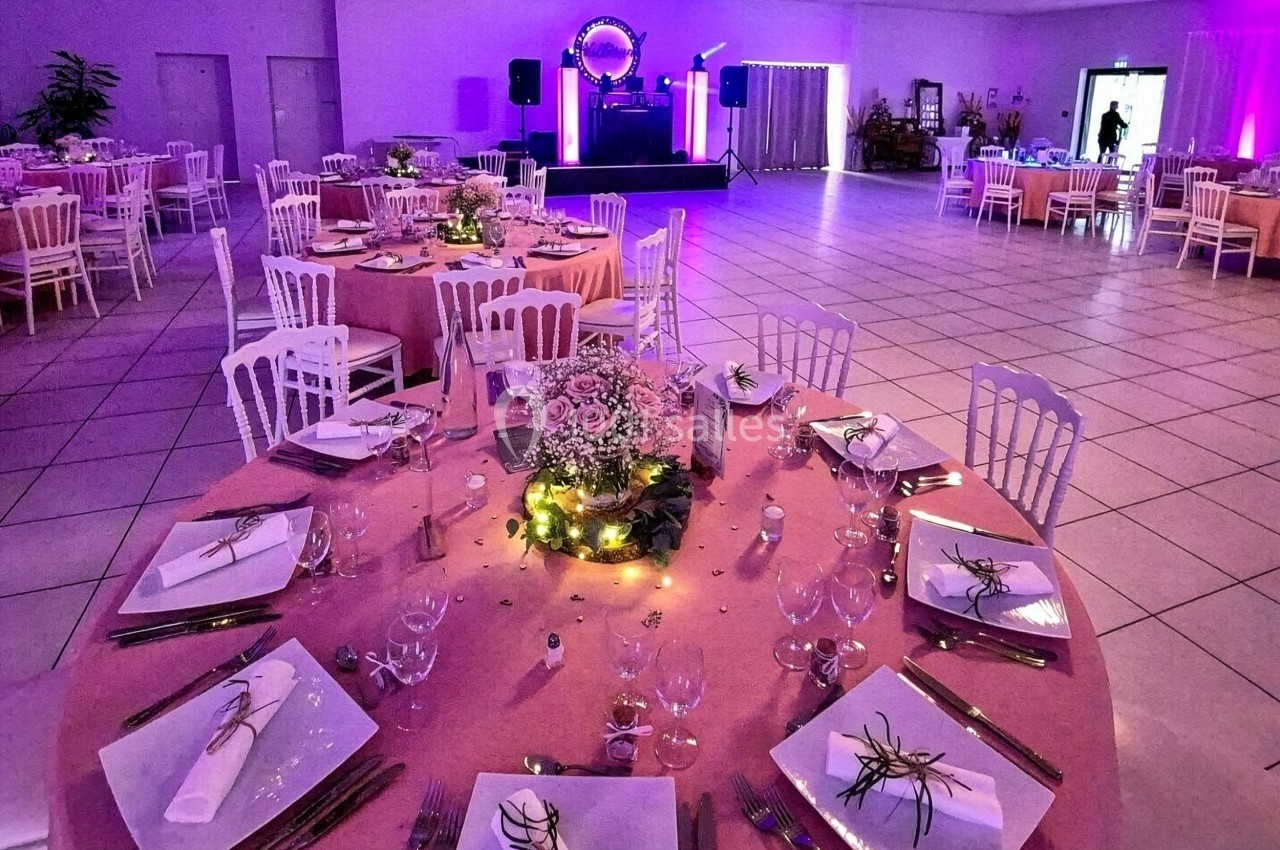 Salle de réception décorée avec des tables rondes élégamment dressées et éclairage d'ambiance violet.
