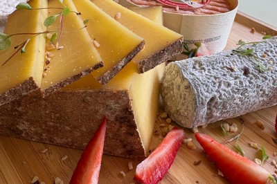 Plateau en bois avec fromages variés, fraises fraîches, noix concassées et herbes décoratives près d'une fenêtre.