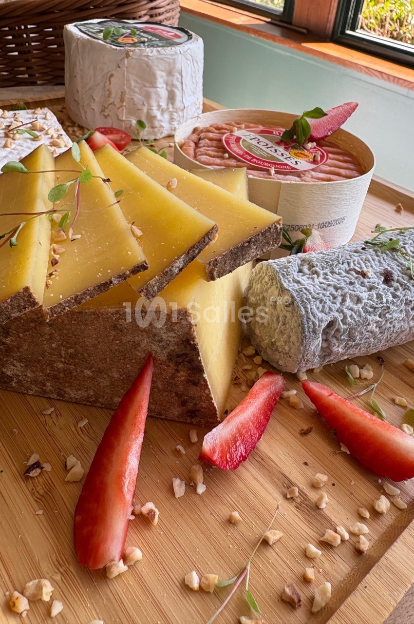 Plateau en bois avec fromages variés, fraises tranchées, noix concassées et herbes fraîches, près d'une fenêtre.