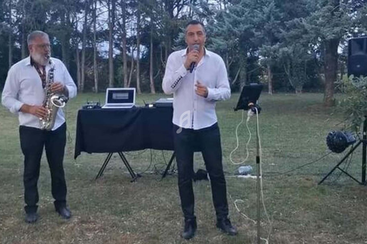 Deux musiciens en plein air, l'un chantant au micro, l'autre jouant du saxophone, avec du matériel audio en arrière-plan.