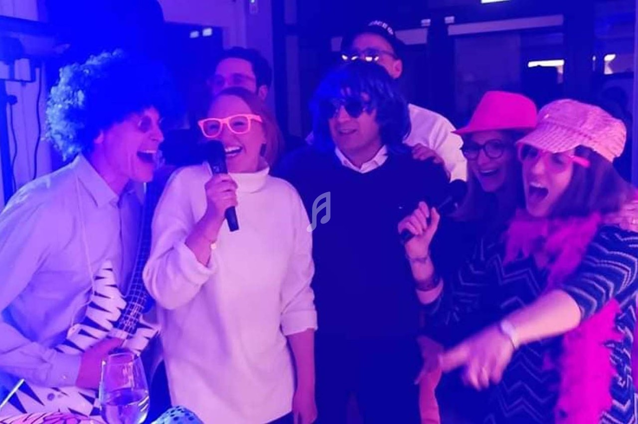 Des personnes déguisées chantent et s'amusent dans une ambiance festive avec éclairage violet.