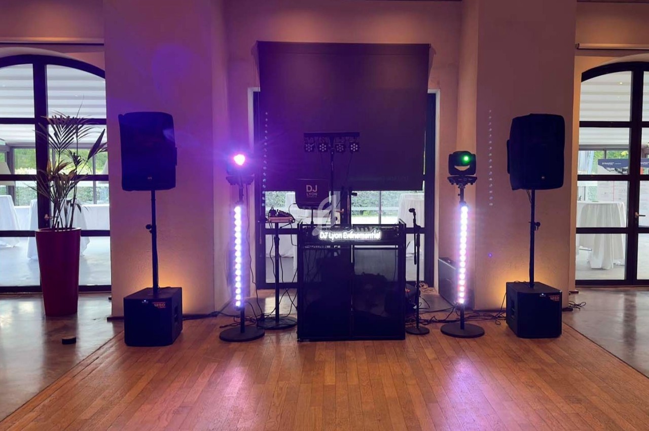 Installation de matériel de DJ avec enceintes, lumières et table de mixage dans une salle lumineuse avec baies vitrées.