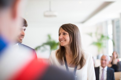 Une femme en robe blanche et talons pose son pied sur un ballon de football sur une pelouse.