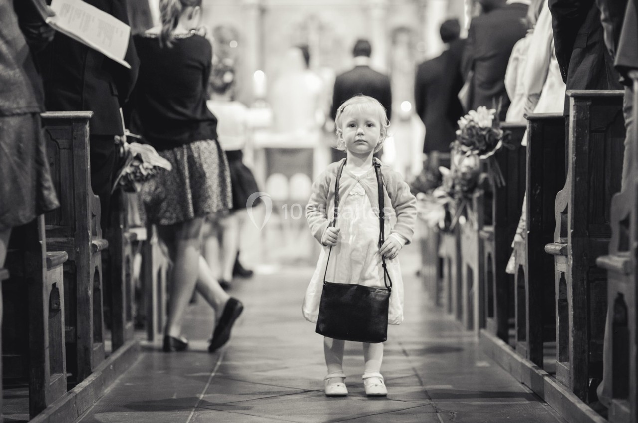 Un enfant debout dans l'allée centrale d'une église, entouré d'adultes assis sur des bancs.