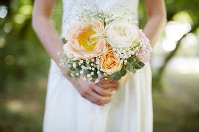 Une femme en robe blanche et talons pose son pied sur un ballon de football sur une pelouse.