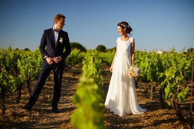 Une femme en robe blanche et talons pose son pied sur un ballon de football sur une pelouse.