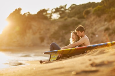 Une femme en robe blanche et talons pose son pied sur un ballon de football sur une pelouse.