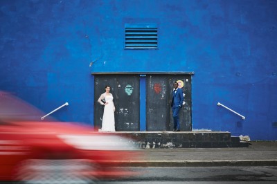 Une femme en robe blanche et talons pose son pied sur un ballon de football sur une pelouse.