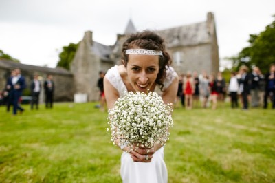 Une femme en robe blanche et talons pose son pied sur un ballon de football sur une pelouse.