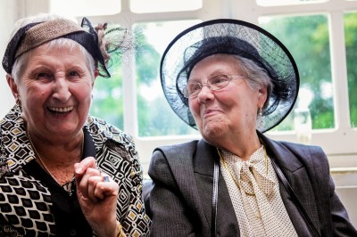 Une femme en robe blanche et talons pose son pied sur un ballon de football sur une pelouse.