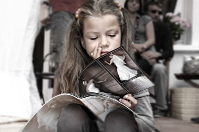 Une femme en robe blanche et talons pose son pied sur un ballon de football sur une pelouse.