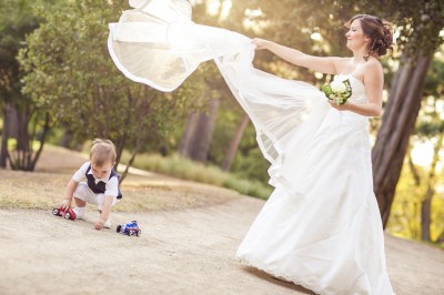 Une femme en robe blanche et talons pose son pied sur un ballon de football sur une pelouse.