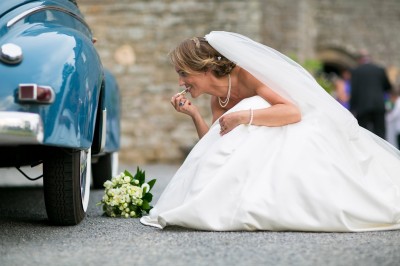 Une femme en robe blanche et talons pose son pied sur un ballon de football sur une pelouse.