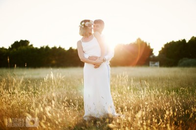 Une femme en robe blanche et talons pose son pied sur un ballon de football sur une pelouse.