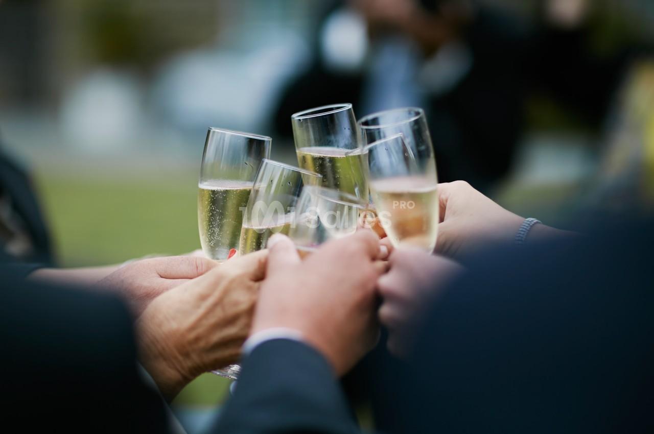 Des mains tenant des flûtes de champagne s'entrechoquent lors d'un toast en extérieur.