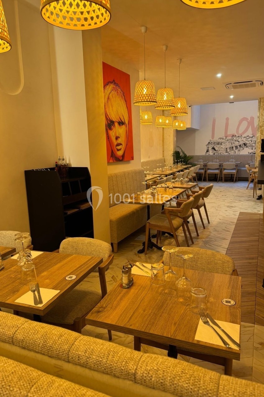 Salle de restaurant chaleureuse avec tables en bois, chaises rembourrées, luminaires suspendus et décoration murale colorée.