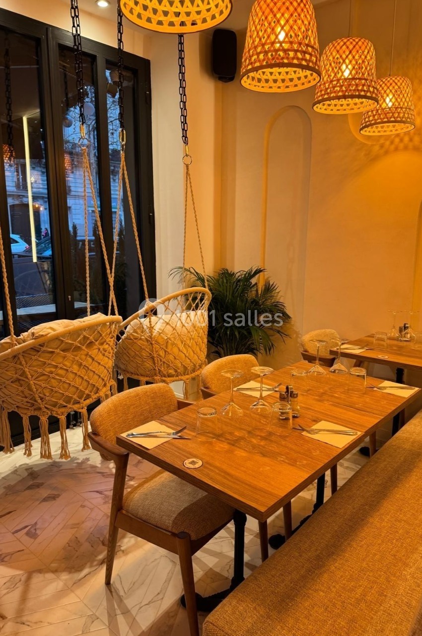 Salle de restaurant chaleureuse avec table en bois, chaises, balançoires suspendues et éclairage tamisé.