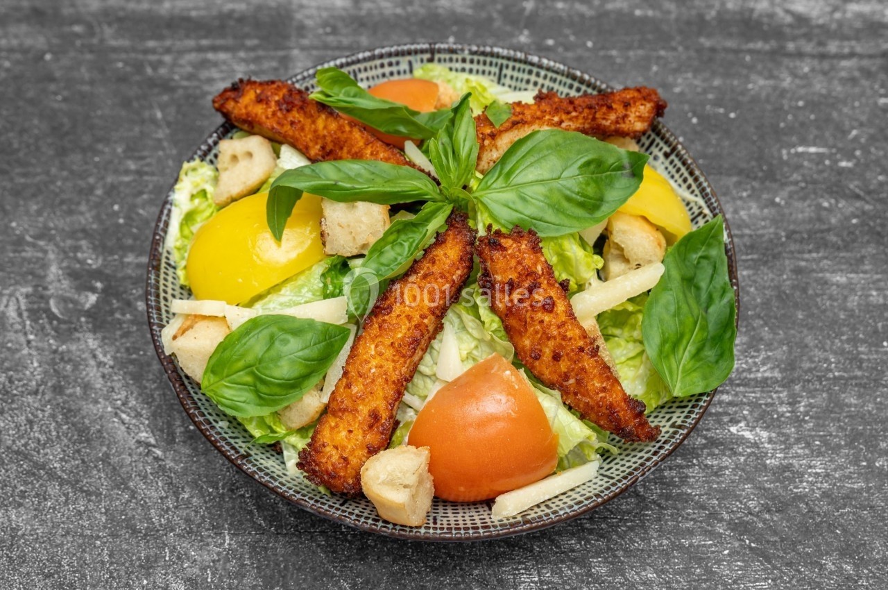 Assiette de salade composée avec filets de poulet panés, tomates, croûtons, feuilles de basilic et poivrons jaunes.