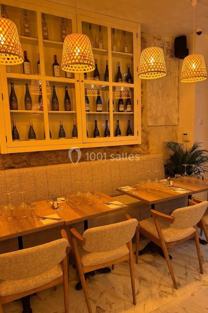 Salle de restaurant chaleureuse avec tables en bois, chaises rembourrées et étagère vitrée contenant des bouteilles de vin.