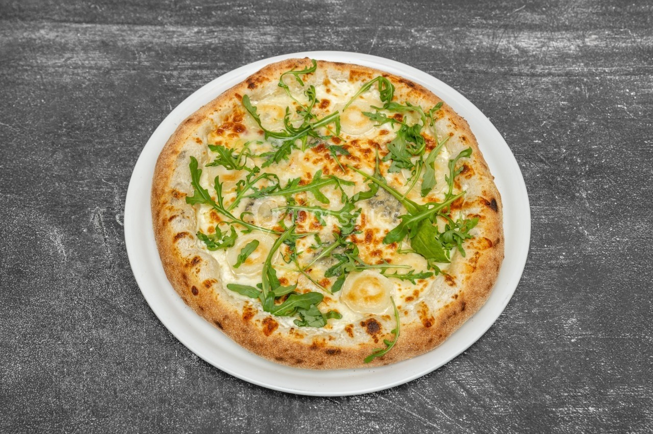 Pizza blanche garnie de roquette et fromage, servie sur une assiette blanche posée sur une table sombre.