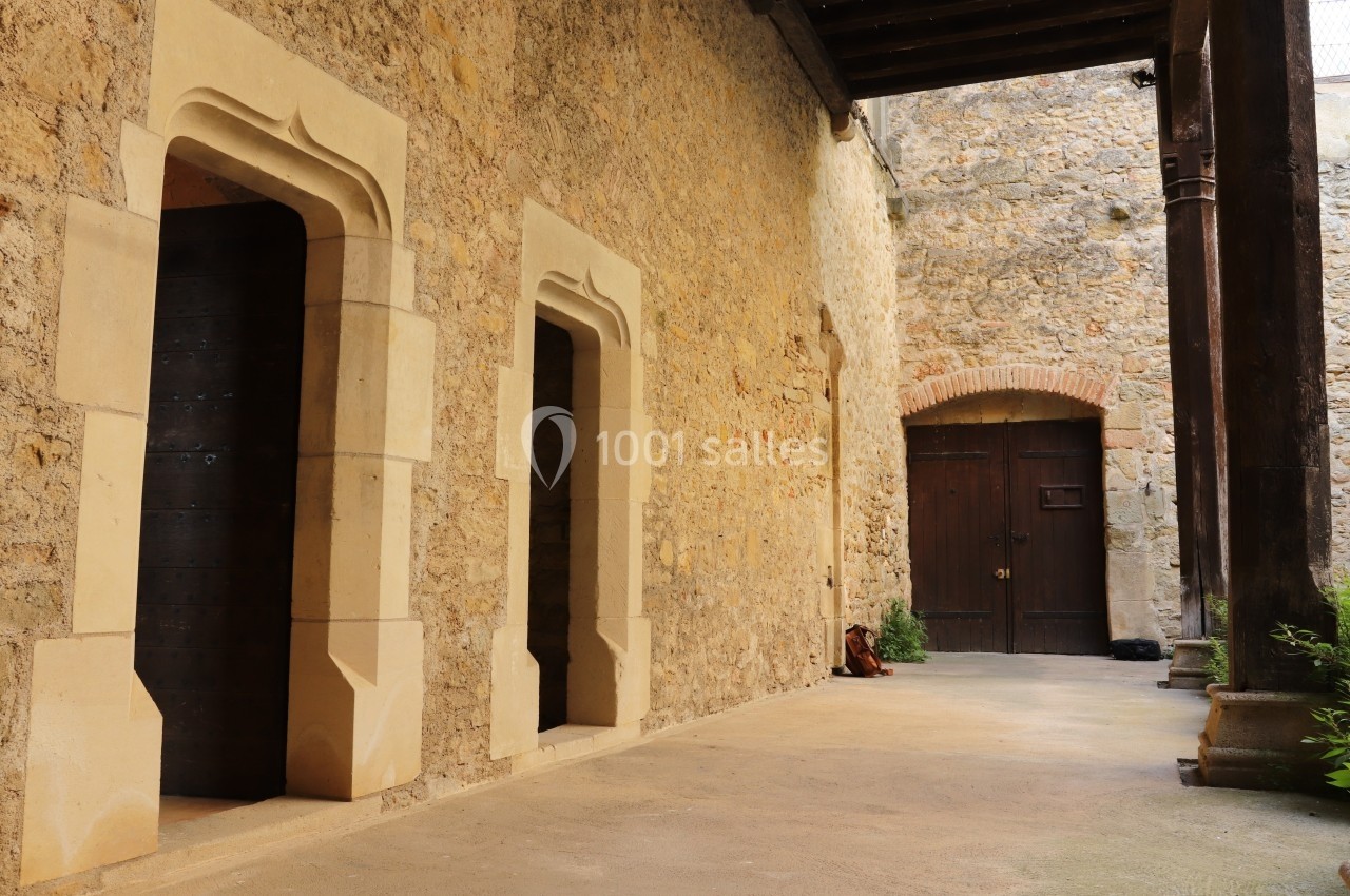 Passage en pierre avec deux ouvertures sculptées et une porte en bois, éclairé par une lumière naturelle.