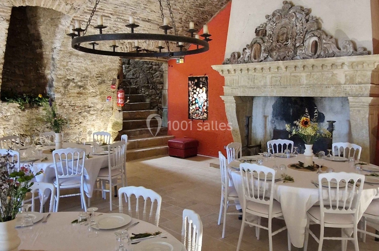 Salle voûtée en pierre avec tables dressées, cheminée ornée et lustre suspendu, décorée pour un événement.