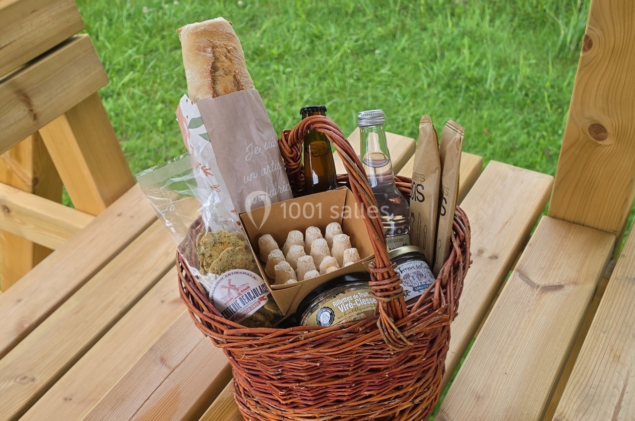 Panier en osier contenant du pain, des biscuits, des boissons et divers produits alimentaires, posé sur une table en bois.