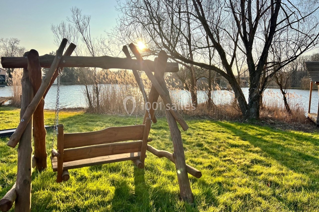 Balançoire en bois sur une pelouse ensoleillée, près d'un lac entouré d'arbres en hiver.