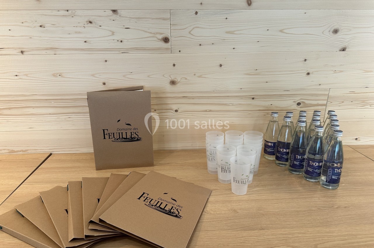 Des dossiers en carton, des gobelets réutilisables et des bouteilles d'eau disposés sur une table en bois clair.