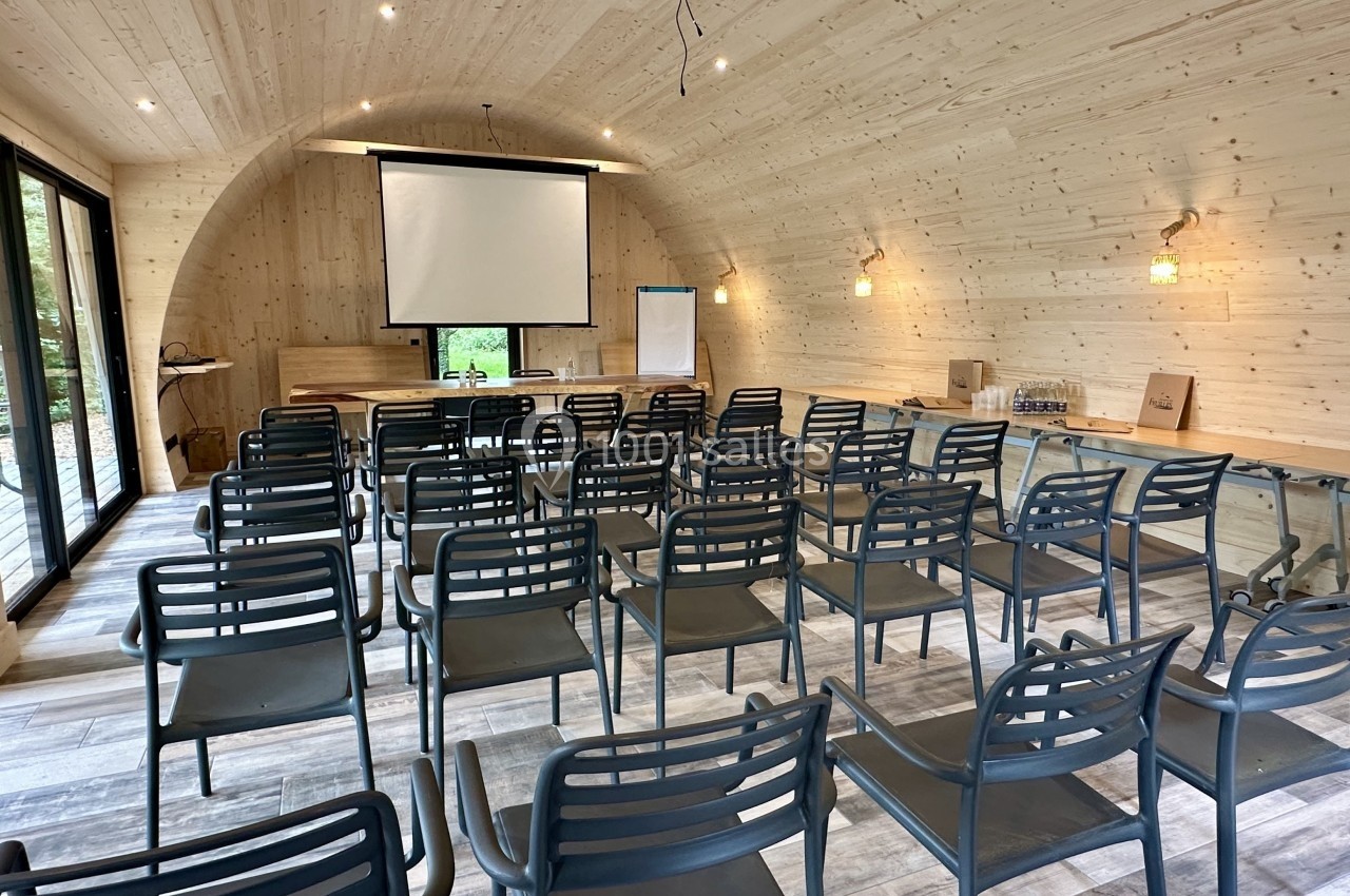 Salle de réunion en bois avec des rangées de chaises, un écran de projection, un paperboard et des fenêtres donnant sur l…