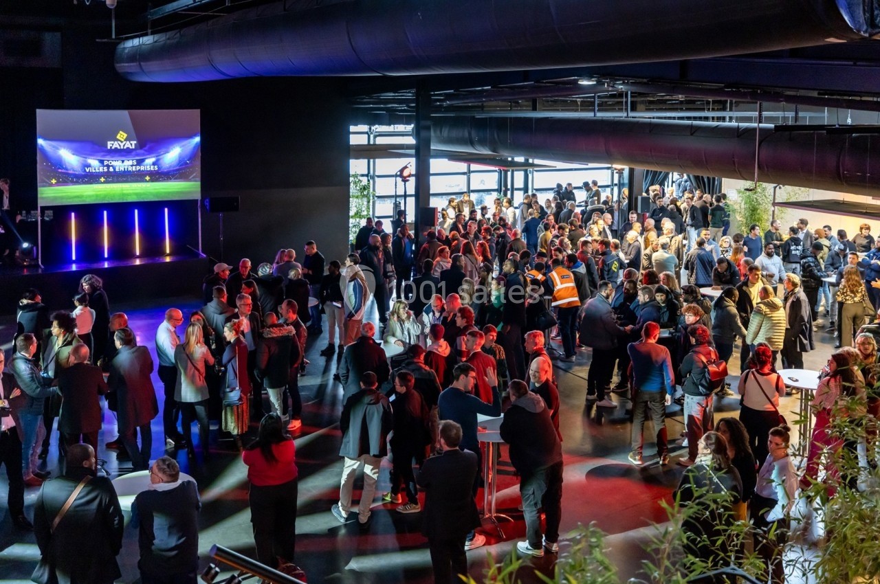 Groupe de personnes rassemblées dans un espace événementiel moderne avec éclairage coloré et écran projeté.