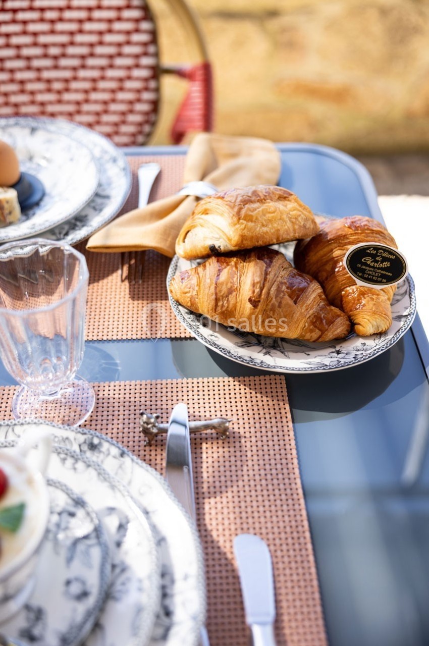 Assiette de croissants sur une table dressée avec vaisselle élégante, nappe tissée et verre transparent.